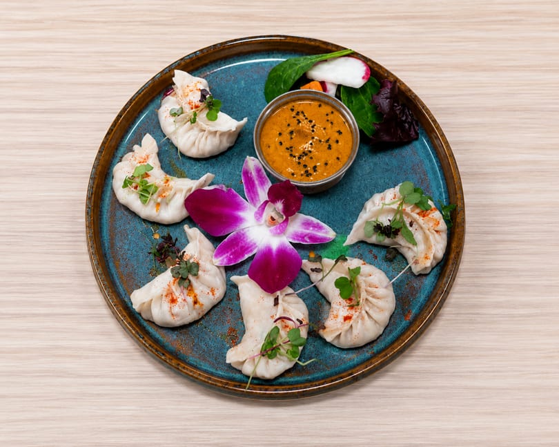 Steamed dumplings with chili flakes and microgreens, served with a peanut dipping sauce and salad.